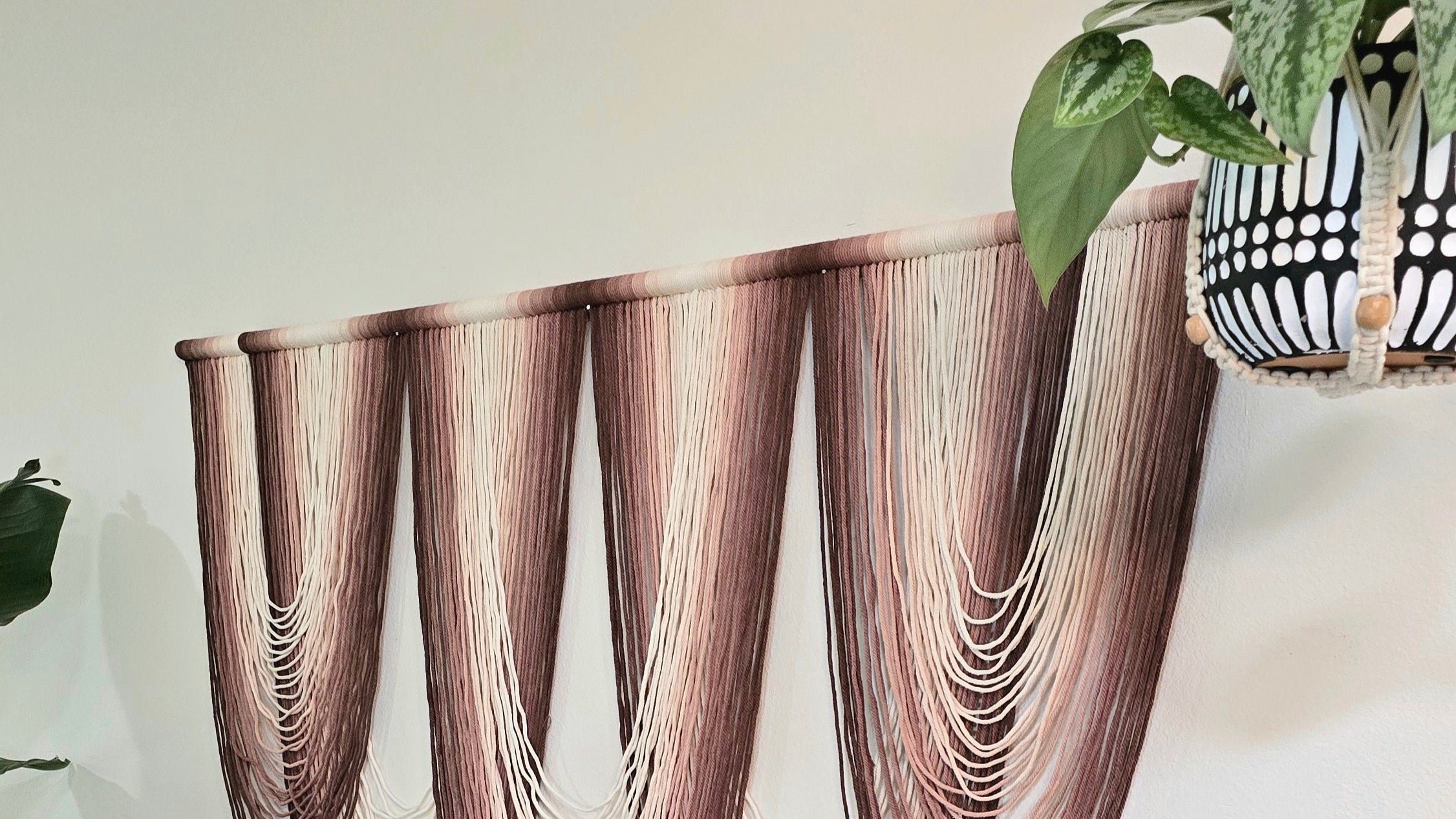 Decorative wall art resembling draped fabric on a white wall with a plant in the corner.